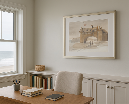 Home office with a desk, chair, books, and a framed picture of a coastal scene.