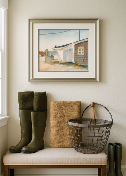 Framed artwork above a bench with green boots, a woven basket, and a wire basket.