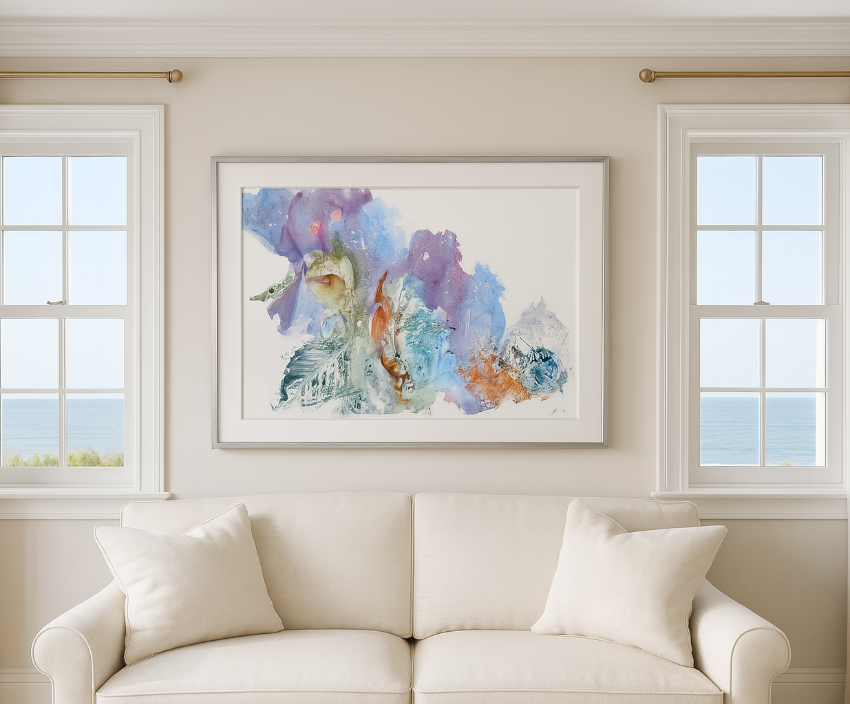 Framed abstract artwork on a wall above a beige sofa with large windows in the background.